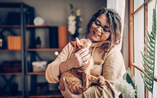 Femme tenant un chat roux dans ses bras, ils se regardent mutuellement, à côté d'une fenêtre.