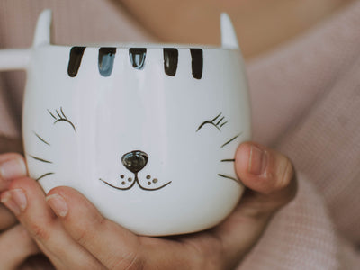 Une tasse chat noir et blanche tenue dans une main