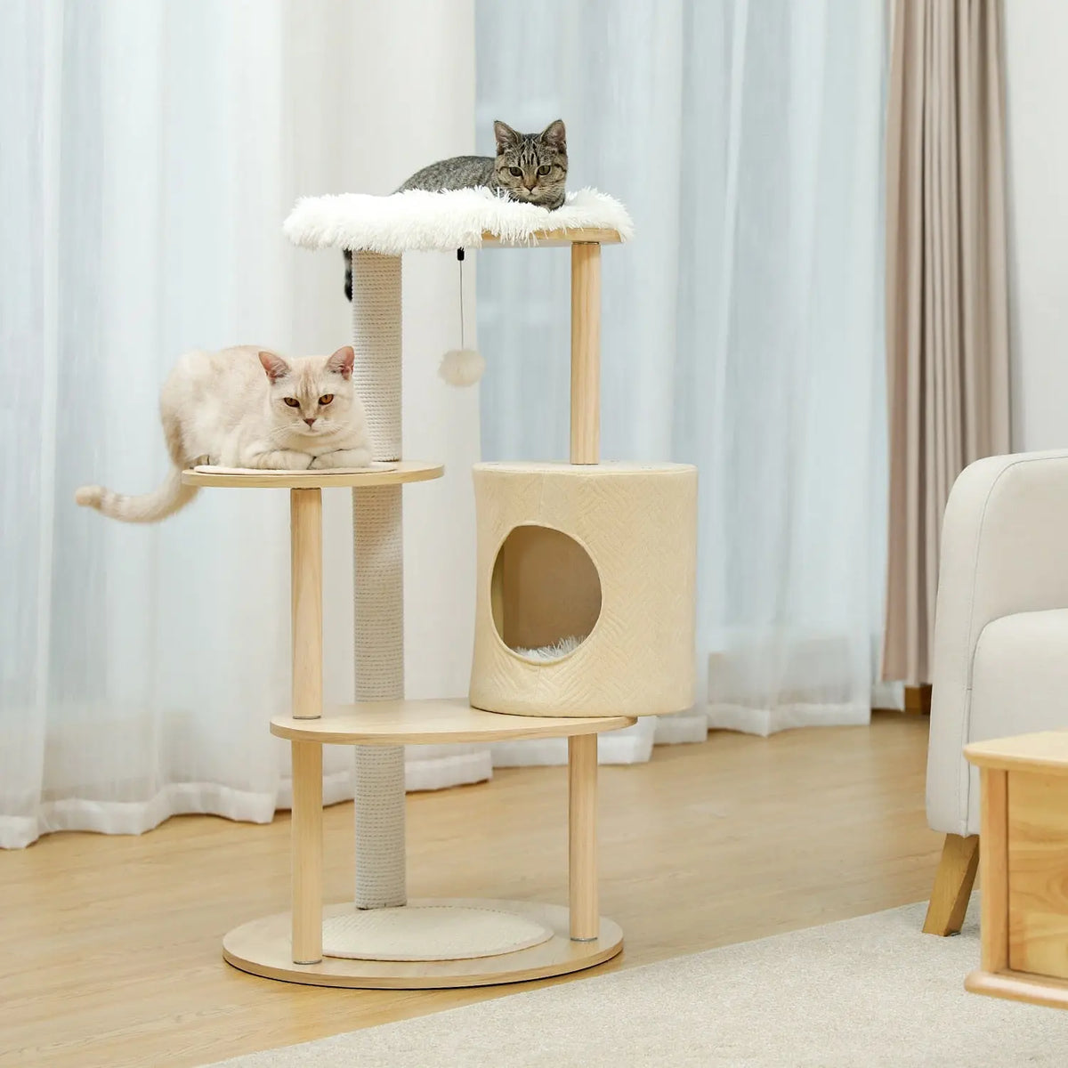 arbre à chat avec deux chats posés en hauteur dans un salon devant des rideaux blancs